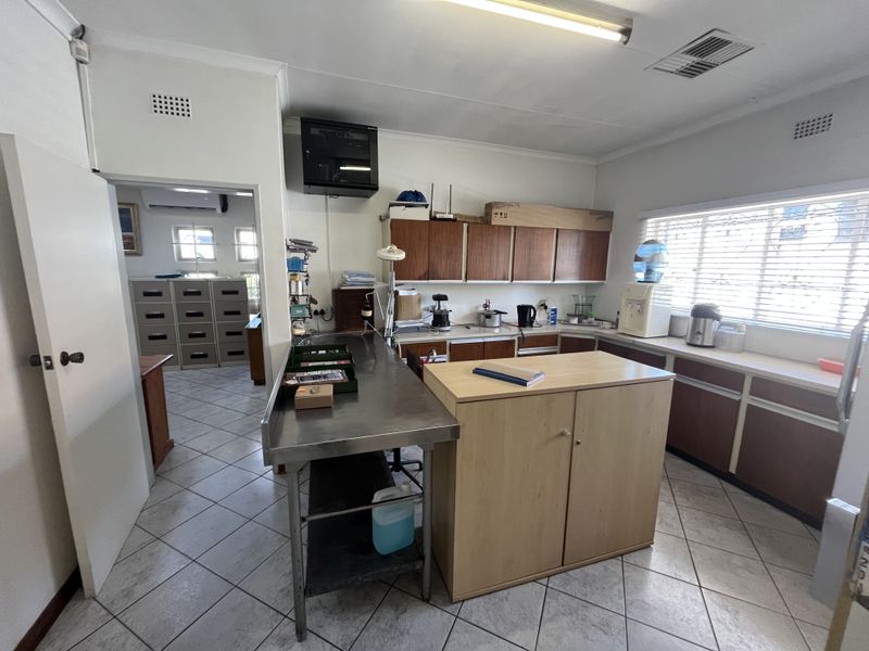 Functional commercial kitchen area featuring stainless steel prep surfaces, built-in cabinetry, and tiled flooring, suitable for office or commercial utility use.