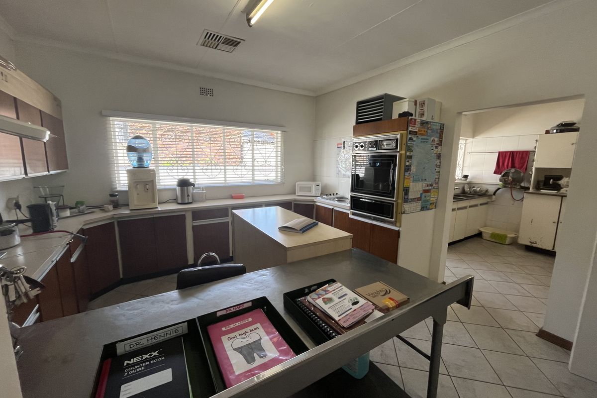 A functional commercial kitchen space featuring built-in cabinetry, a double wall oven, and tiled flooring, with an adjacent scullery area.