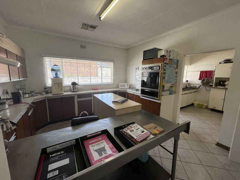 A functional commercial kitchen space featuring built-in cabinetry, a double wall oven, and tiled flooring, with an adjacent scullery area.