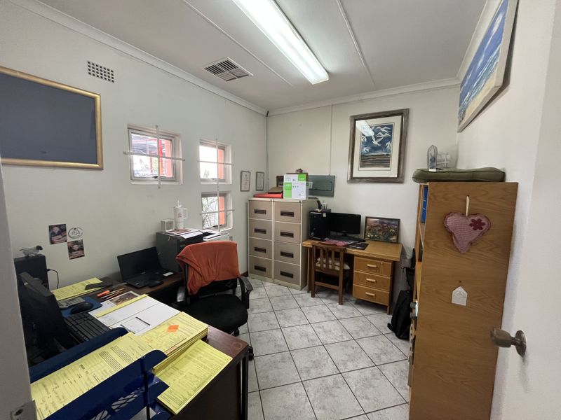 A functional commercial office space featuring tiled flooring, fluorescent lighting, and security-barred windows, providing a practical work environment.
