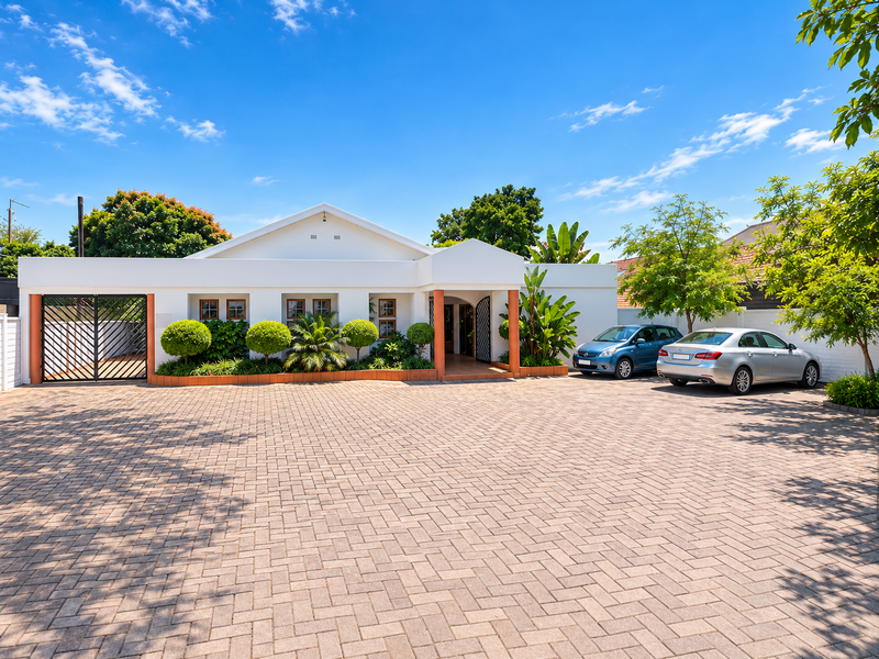 A well-maintained commercial property exterior featuring a spacious paved driveway, secure gated entrance, and established landscaping with a clean, white facade.