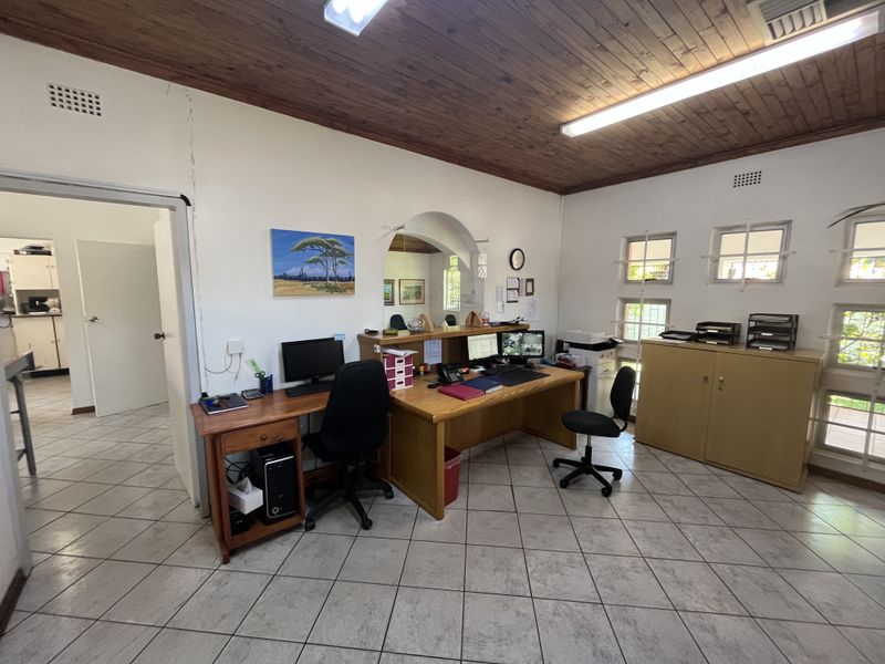 A functional office space featuring a timber ceiling, ceramic tiled flooring, and an arched doorway leading to an adjacent room.