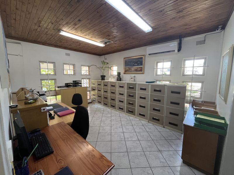A functional office space featuring a timber ceiling, tiled flooring, air conditioning, and multiple windows with security bars.