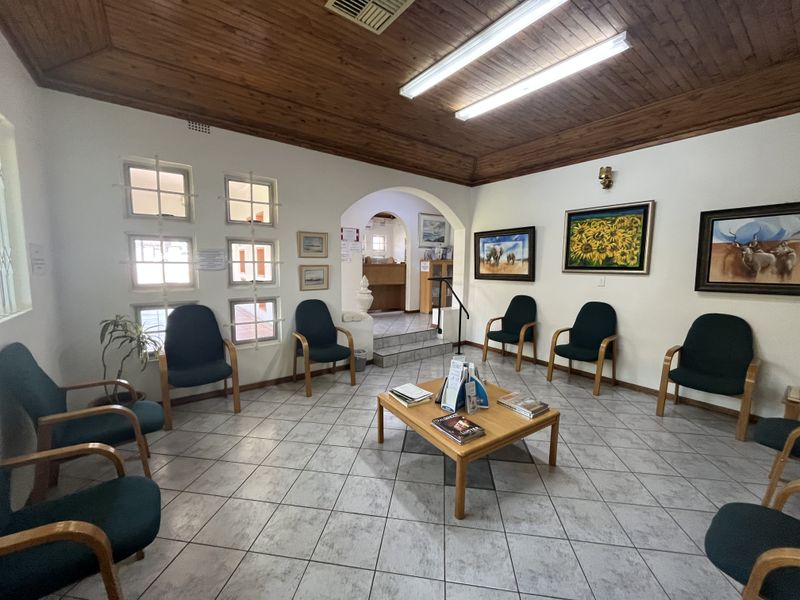 A spacious commercial reception or waiting area featuring ceramic tiled flooring, a timber-paneled ceiling, and an arched transition to an inner office space.