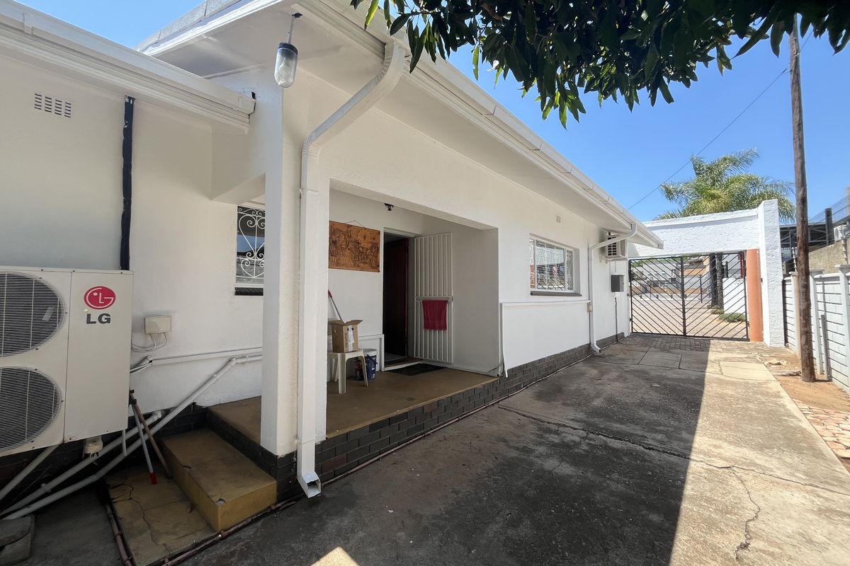 Rear exterior view of the commercial property featuring a concrete driveway, covered patio area, and secure gated access.
