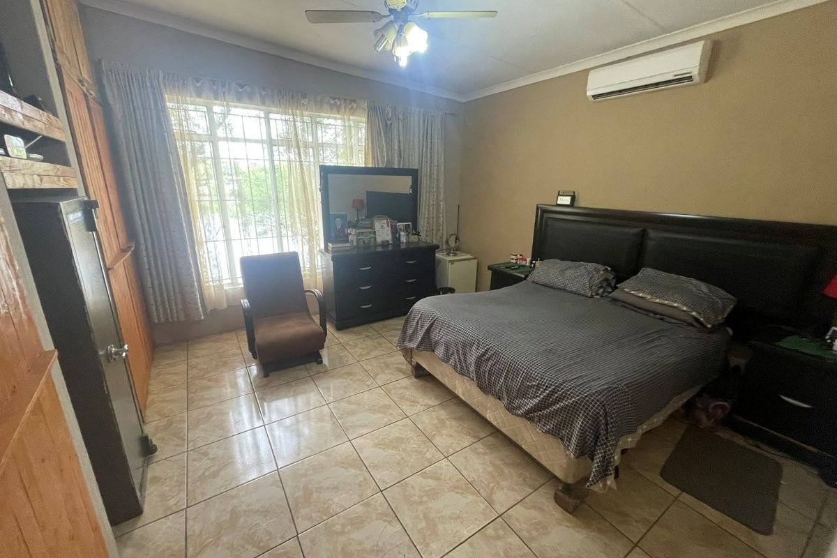 Spacious bedroom featuring tiled flooring, built-in cupboards, a ceiling fan, and a wall-mounted air conditioning unit.