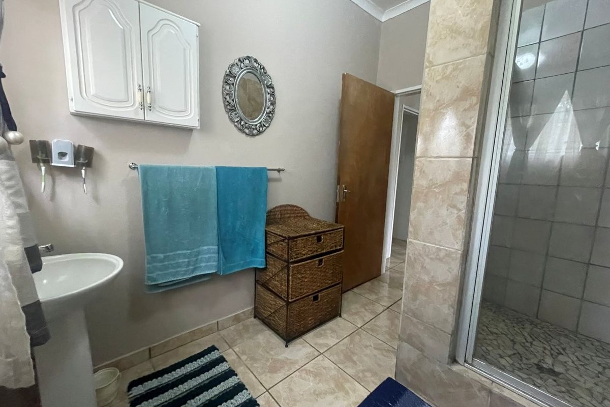 A functional bathroom featuring a pedestal basin, a tiled shower enclosure, and wall-mounted storage cabinetry with neutral floor tiling.