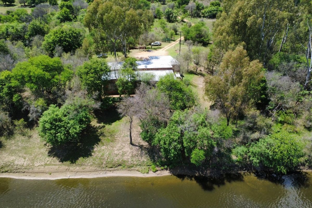 Aerial view of a small holding property featuring a metal-roofed dwelling situated in a wooded area with direct waterfront access.