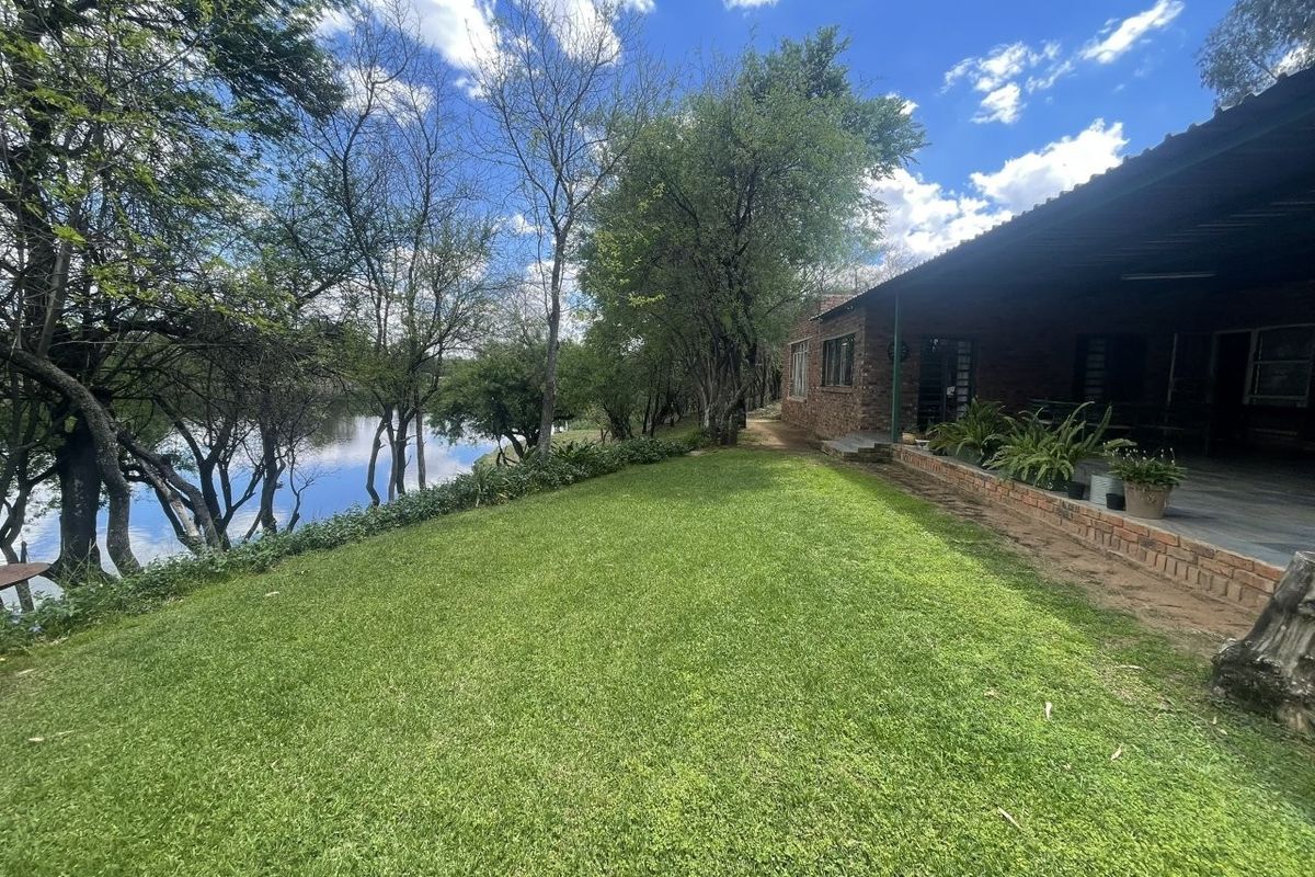 A scenic rear exterior view featuring a well-maintained lawn, a covered brick patio, and direct access to a tranquil waterfront setting.