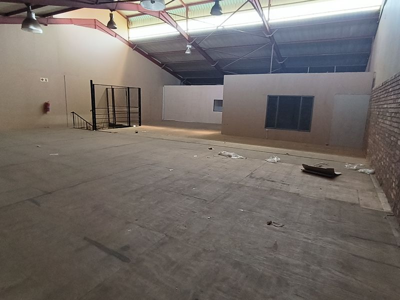 Spacious industrial open-plan area featuring exposed steel roof trusses, a brick feature wall, and functional industrial lighting, suitable for various commercial or warehouse uses.