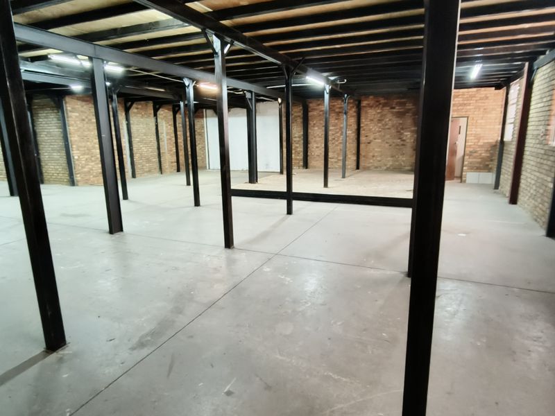 Spacious industrial utility area featuring exposed brick walls, concrete flooring, and a robust steel support structure with overhead beam framing.