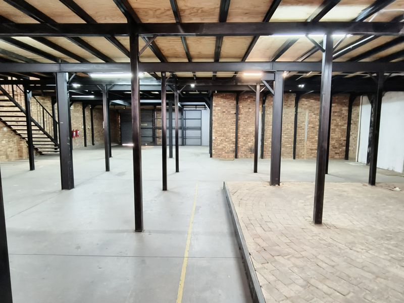 Spacious industrial utility area featuring exposed steel structural beams, brick walls, concrete flooring, and a mezzanine-ready timber ceiling structure.