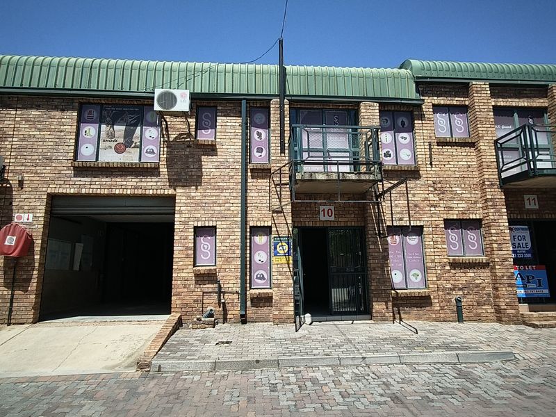 Front elevation of an industrial unit featuring face brick construction, a roller shutter door, and a metal balcony, with paved driveway access.