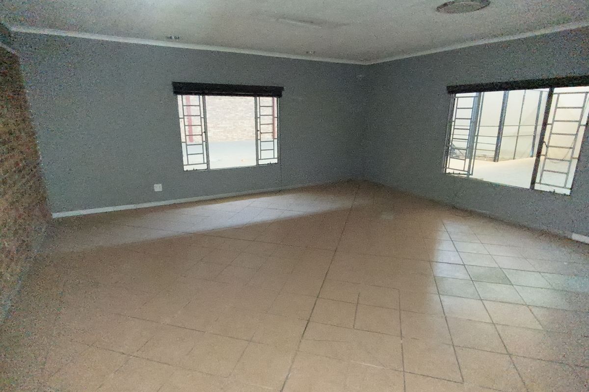 Spacious, empty living area featuring tiled flooring, an exposed brick feature wall, and large steel-framed windows providing ample natural light.