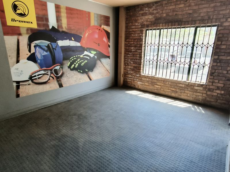 Empty office space featuring exposed brick walls, rubber flooring, and a window with security bars.