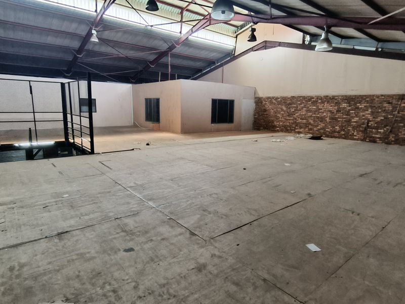 Spacious industrial mezzanine area featuring exposed steel roof trusses, industrial lighting, and a combination of brick and painted wall finishes.