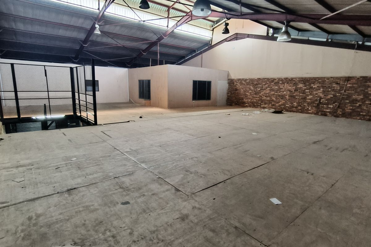 Spacious industrial mezzanine area featuring exposed steel roof trusses, industrial lighting, and a combination of brick and painted wall finishes.