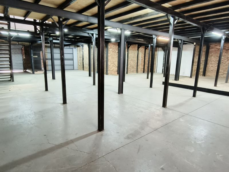 Spacious industrial utility area featuring exposed brick walls, concrete flooring, and a steel mezzanine structure with an integrated metal staircase.