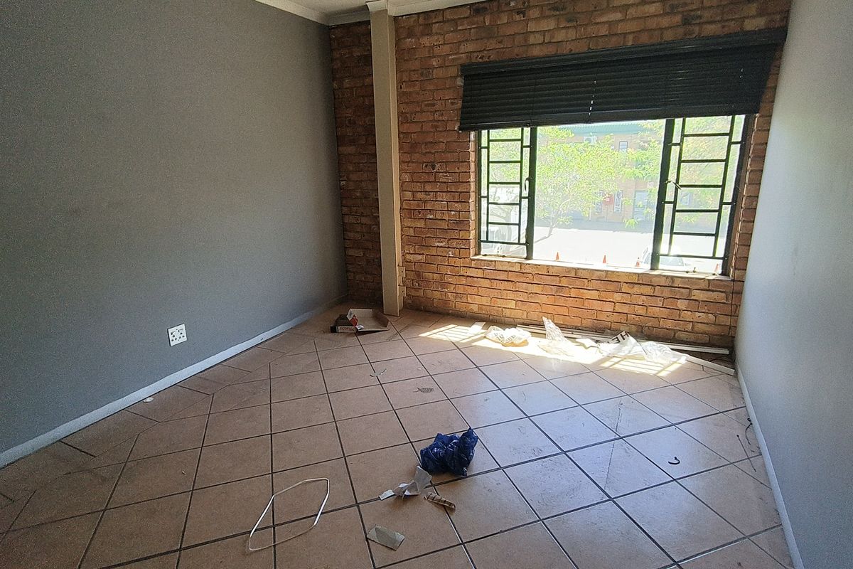 An empty bedroom featuring an exposed brick feature wall, tiled flooring, and large metal-framed windows with a fitted blind.