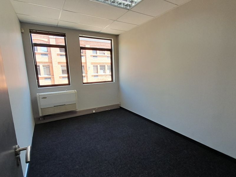 A clean, empty office space featuring dark carpeting, a suspended ceiling with recessed lighting, and an integrated air conditioning unit.