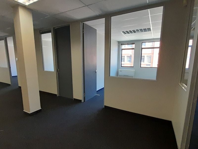An empty office space featuring carpet flooring, suspended ceilings with recessed lighting, and glass partition walls creating a professional, open-plan work environment.
