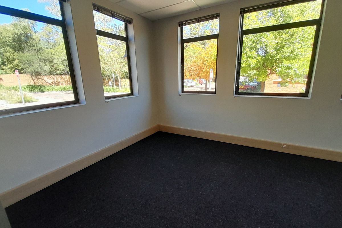 A bright, empty office space featuring large windows providing natural light, dark carpeting, and neutral wall finishes, suitable for a professional workspace.
