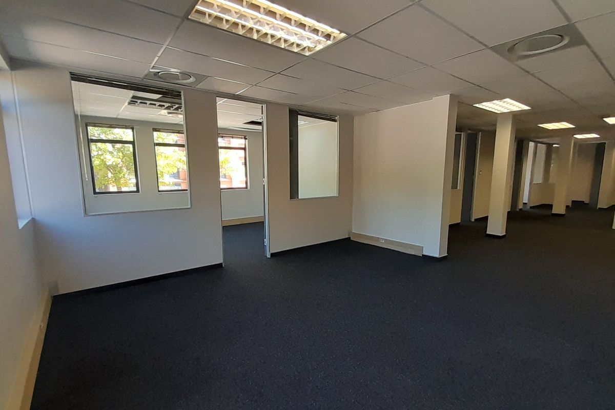Spacious open-plan office area featuring suspended ceilings, recessed lighting, carpeted flooring, and internal glass partitions, offering a versatile workspace layout.