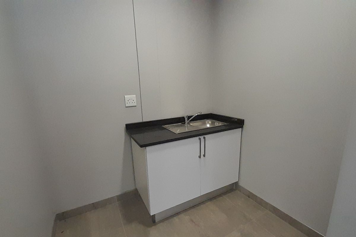 A compact kitchenette area featuring a modern base cabinet, integrated sink, and dark countertop, suitable for office staff use.