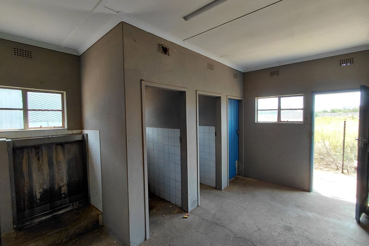 A utilitarian industrial washroom facility featuring a wall-mounted urinal, multiple partitioned cubicle entrances, and direct exterior access.