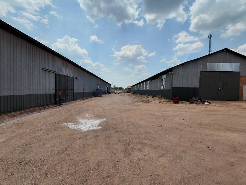 Exterior view of an industrial property featuring two large metal-clad warehouse buildings with a central unpaved access yard.