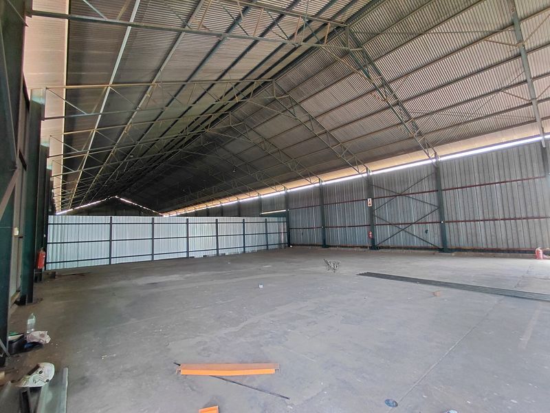 Spacious industrial warehouse featuring high-clearance steel truss roofing, corrugated metal wall cladding, and a durable concrete floor, suitable for storage or manufacturing operations.