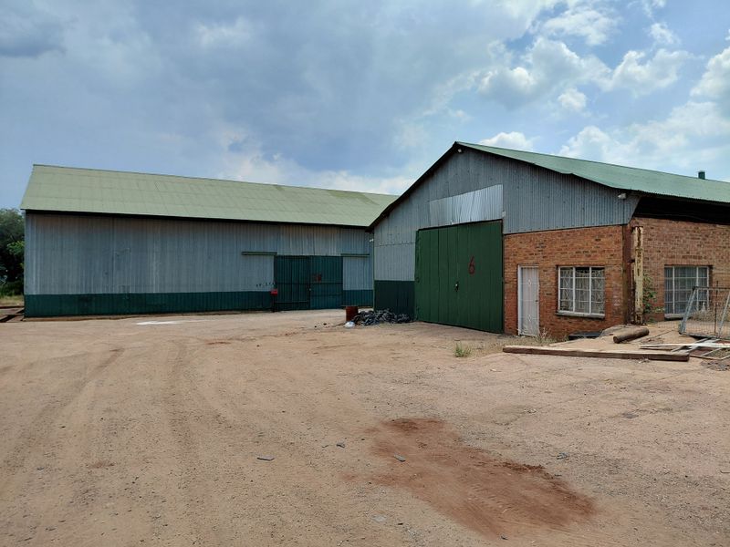 Industrial property featuring two large warehouse structures with corrugated metal roofing, sliding access doors, and brick masonry exterior walls.