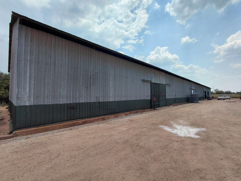 Exterior view of a large industrial warehouse featuring corrugated metal cladding and sliding access doors, situated on a gravel lot.