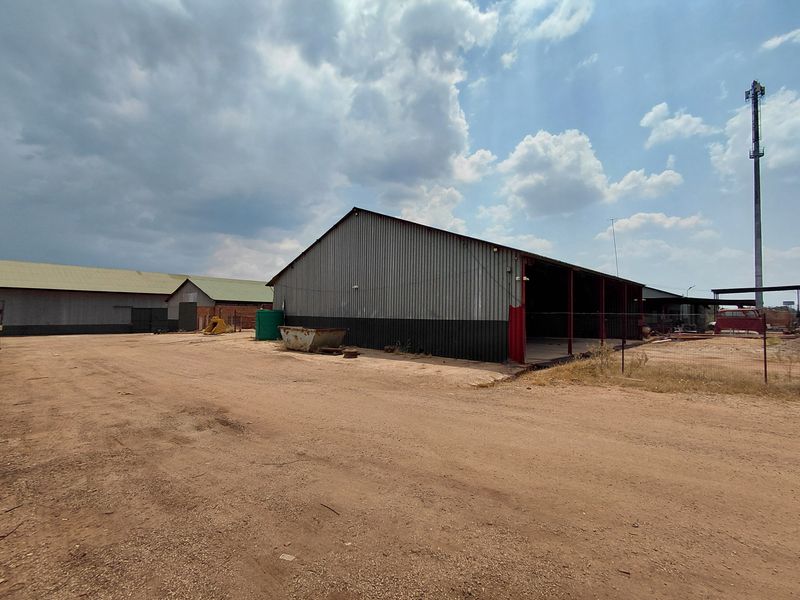 Industrial property featuring large corrugated metal warehouse structures with open-bay access and expansive unpaved yard space.