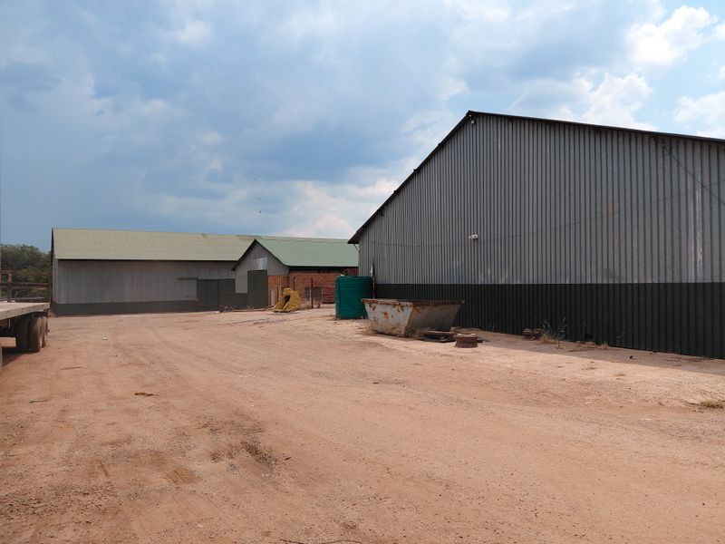 Industrial property featuring large corrugated metal warehouses with expansive unpaved yard space, suitable for storage or logistics operations.