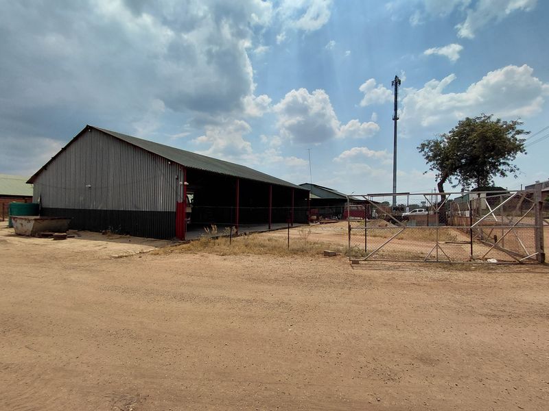 Industrial property featuring a large corrugated metal warehouse structure with open bays, set on an unpaved lot with perimeter fencing.
