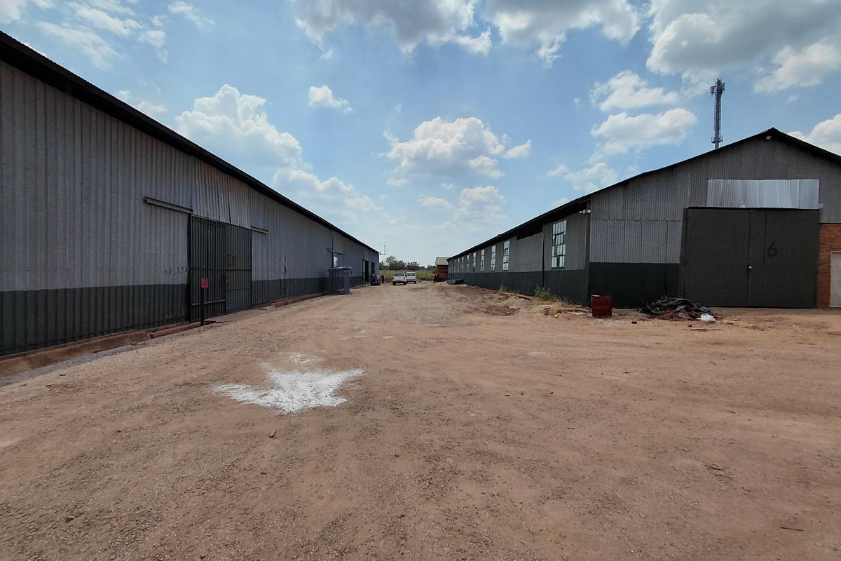 Exterior view of an industrial property featuring two large metal-clad warehouse buildings with a central unpaved access yard.