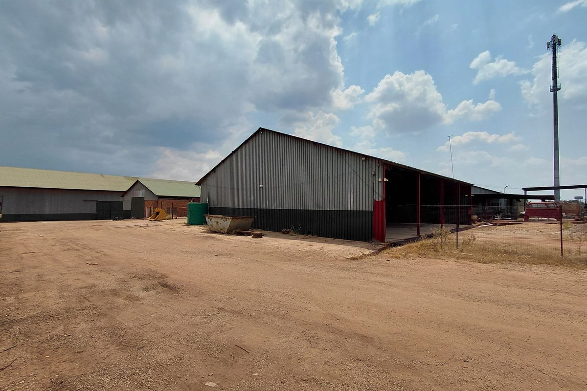 Industrial property featuring large corrugated metal warehouse structures with open-bay access and expansive unpaved yard space.