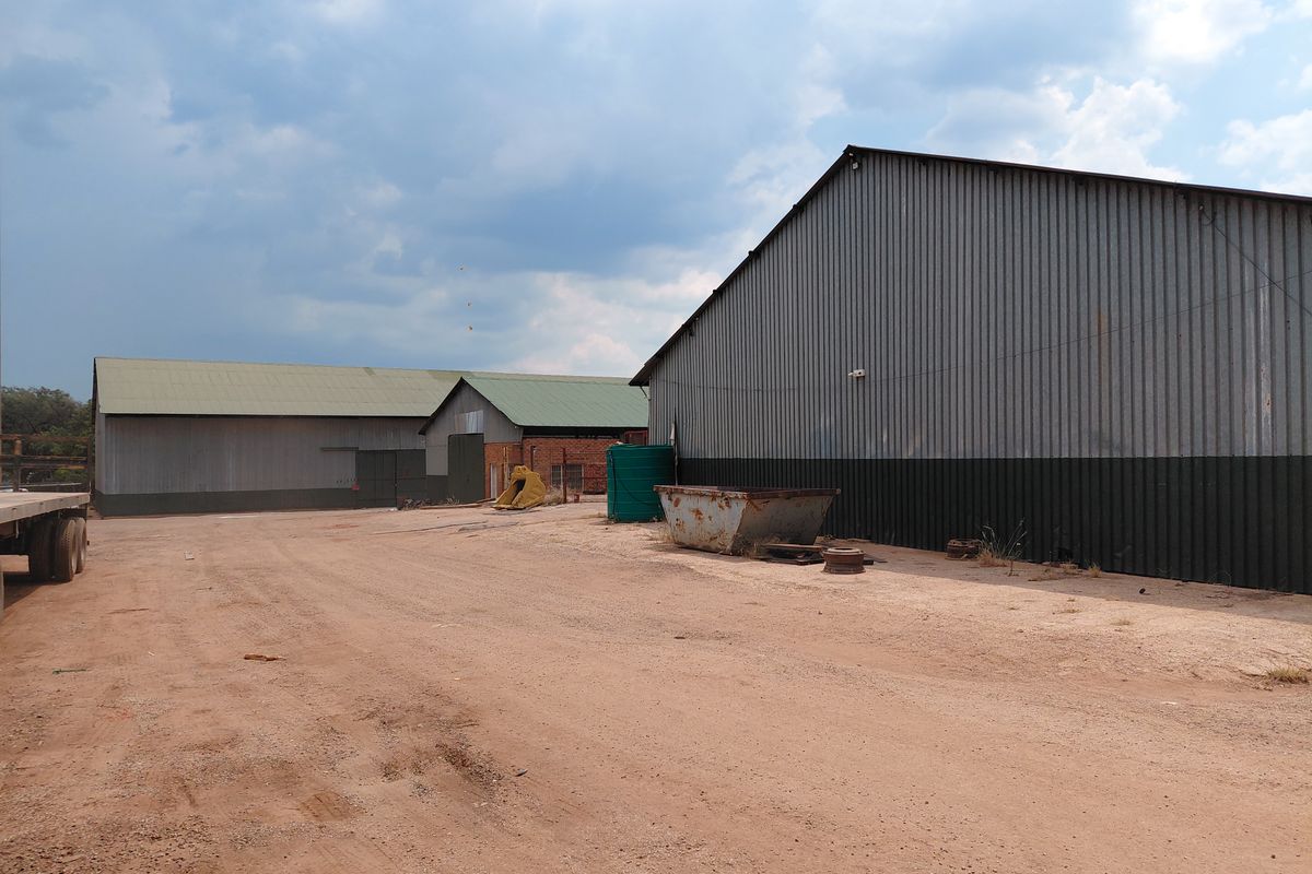 Industrial property featuring large corrugated metal warehouses with expansive unpaved yard space, suitable for storage or logistics operations.