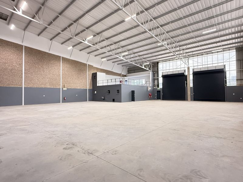 Spacious industrial warehouse featuring high ceilings, concrete flooring, multiple roller shutter doors, and a mezzanine level, suitable for various commercial or storage operations.