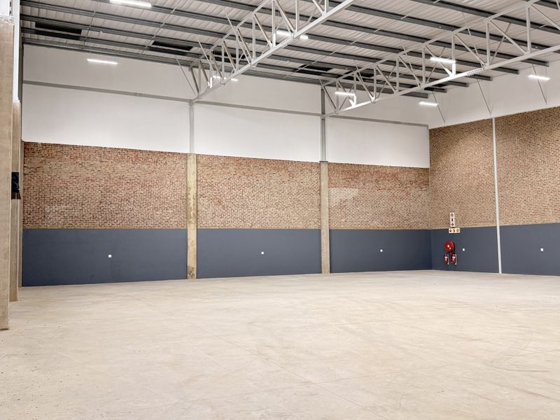 Spacious industrial warehouse unit featuring high ceilings with exposed steel trusses, durable concrete flooring, and brick wall finishes.