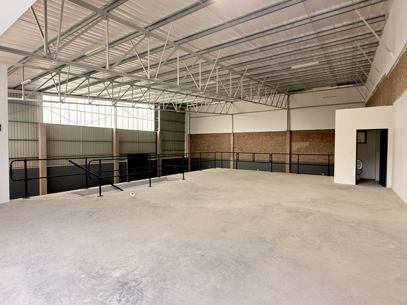 Spacious industrial mezzanine level featuring exposed steel roof trusses, concrete flooring, and metal safety railings, suitable for storage or office conversion.