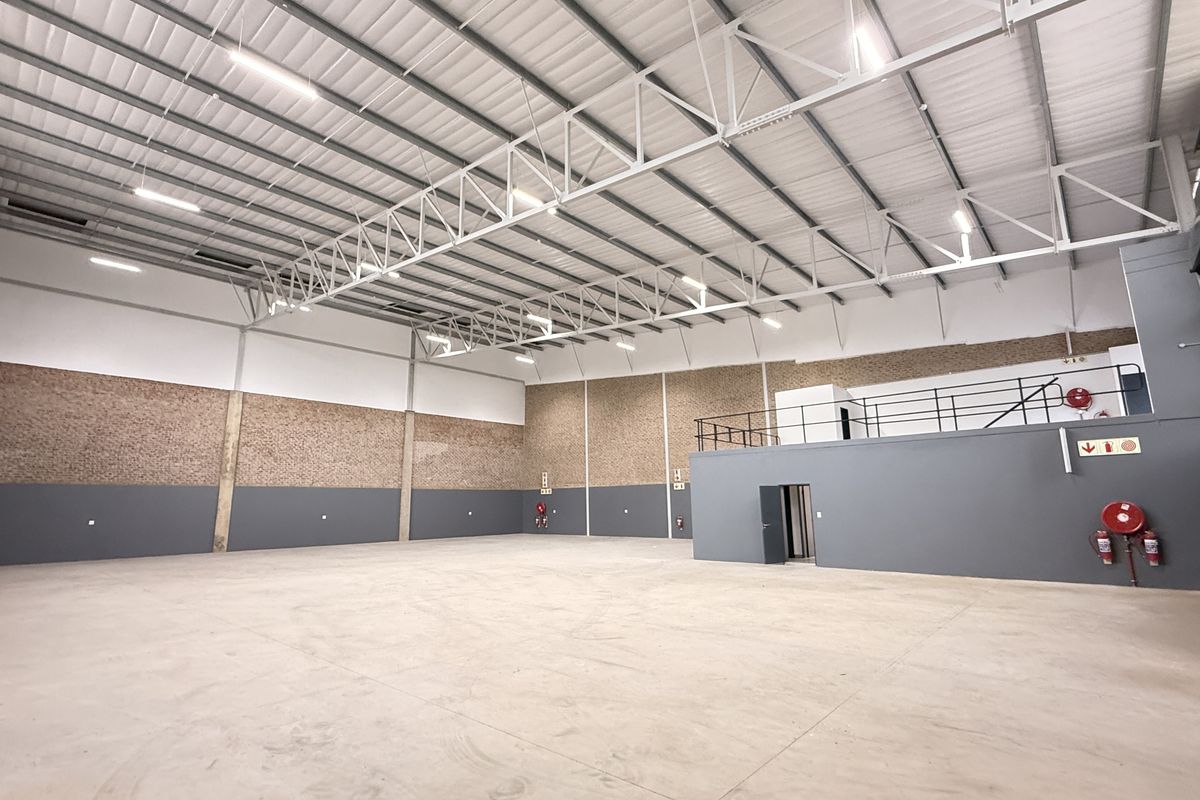Spacious industrial warehouse featuring high ceilings with exposed steel trusses, polished concrete flooring, a mezzanine level, and integrated fire safety equipment.