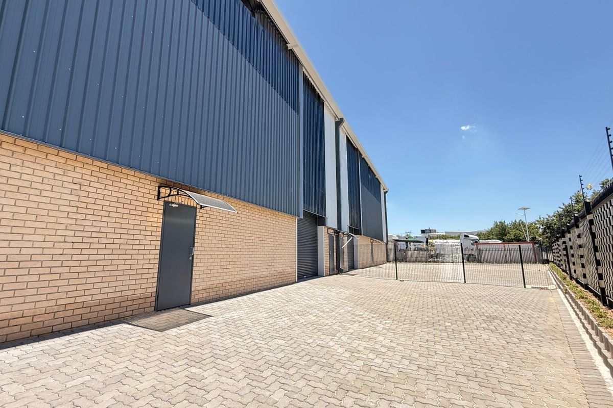 A well-maintained industrial exterior featuring a brick and metal facade, paved yard area, and secure perimeter fencing with an electric security system.