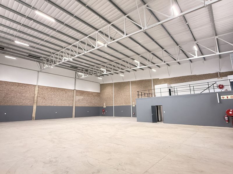 Spacious industrial warehouse featuring high ceilings with exposed steel trusses, polished concrete flooring, a mezzanine level, and integrated fire safety equipment.