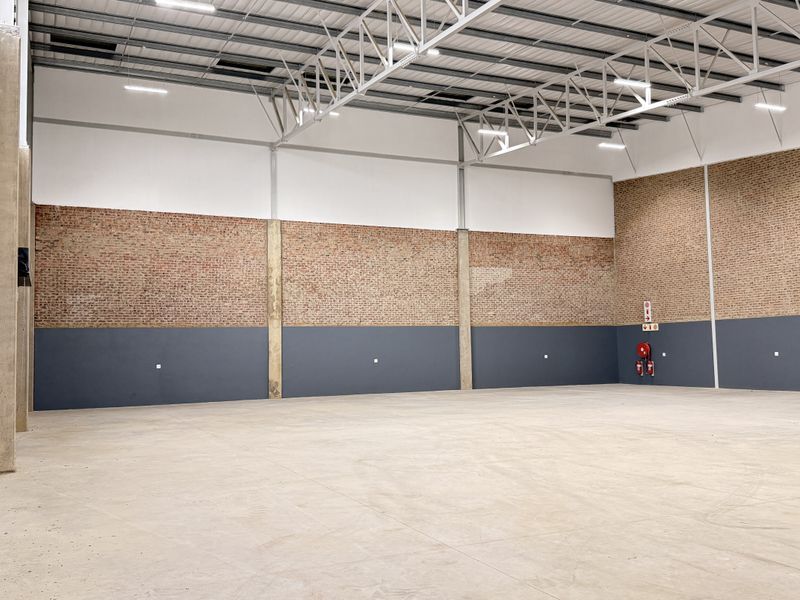 Spacious industrial warehouse unit featuring high ceilings, exposed brick walls, durable concrete flooring, and functional high bay lighting.