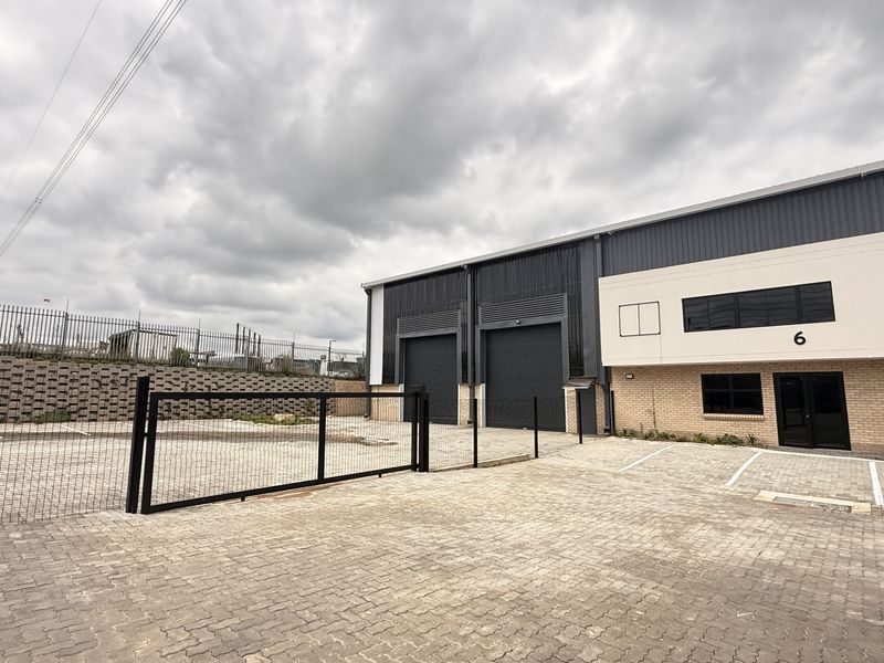 Modern industrial unit featuring roller shutter doors, paved parking area, and secure perimeter fencing in a well-maintained business park setting.