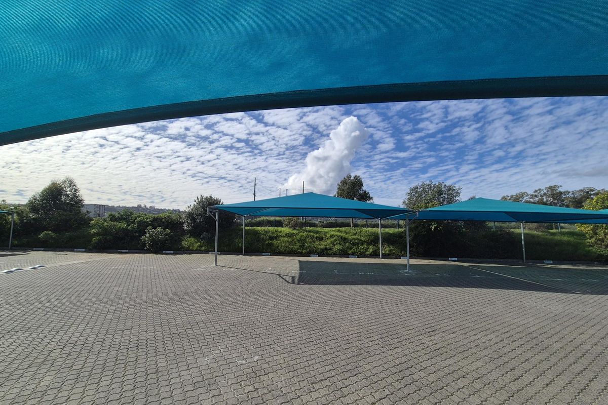Outdoor parking area featuring paved ground and multiple shade cloth structures for vehicle protection.