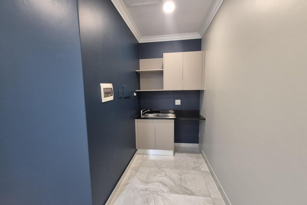 A compact office kitchenette featuring modern cabinetry, a stainless steel sink, dark stone countertop, and tiled flooring.