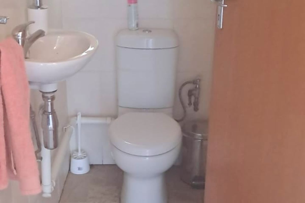 A compact office restroom featuring a wall-mounted basin, a standard toilet, and tiled flooring.